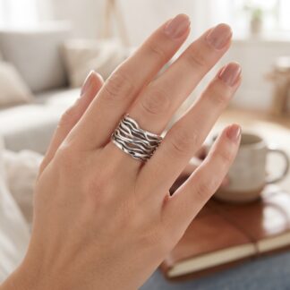 Close-up of a hand with a silver wavy-band ring on the middle finger; soft, neutral background blurred.