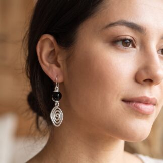 Close-up of a woman's face focusing on her left ear, showing a silver spiral dangling earring and smooth skin near the jawline.