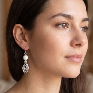 Close-up of a woman's face in profile, highlighting her brown eye, ear, and a silver spiral earring with a pearl bead.
