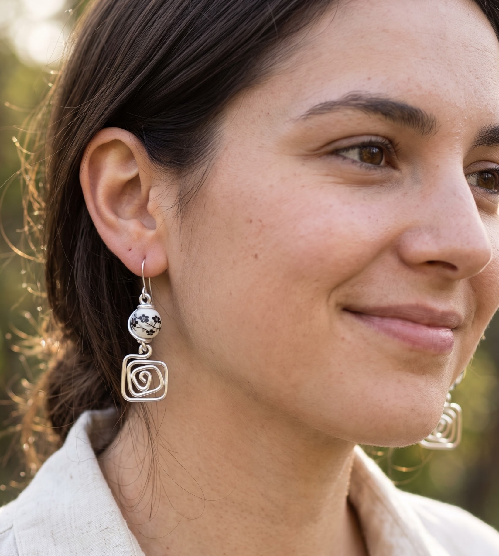 1792572890516 - Zanghi collection Close-up of a woman's ear and silver geometric earrings, with hair tucked behind the ear outside.