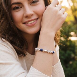 1792573172734 - Zanghi collection Close-up of a smiling woman outdoors, showing a silver and navy beaded bracelet on her wrist.