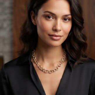 Close-up portrait of a woman with dark wavy hair, wearing a gold chain necklace and a black blouse, neutral expression.