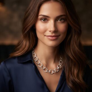 Close-up portrait of a woman with brown hair, wearing a silver chain necklace and a dark navy blouse, warm blurred background.
