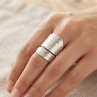 Close-up of a hand wearing two wide hammered silver rings on the middle finger against a neutral background.