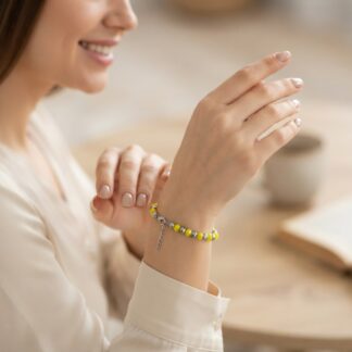 Woman smiling while showing off a yellow and gray beaded bracelet on her wrist with a delicate chain.