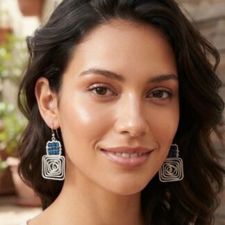 Close-up of a smiling woman with dark wavy hair wearing large silver square spiral earrings.