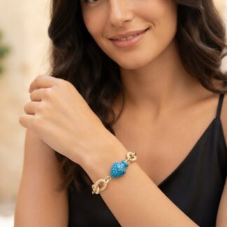 Woman wearing a gold knot bracelet with a bright blue bead on her wrist.