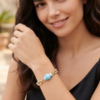 Close-up of a woman's wrist showcasing a gold braided bracelet with a light blue bead charm.