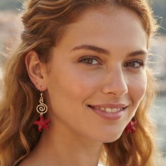 Smiling woman with wavy red hair wearing red starfish earrings outdoors.