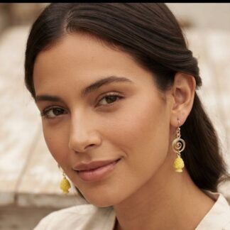 Close-up portrait of a woman with dark hair wearing yellow beaded drop earrings and natural makeup, neutral background.
