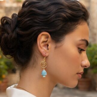 Side profile of a woman with an updo, wearing a gold spiral dangle earring with a blue beaded tassel outdoors.