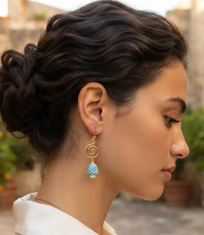 1791826761176 - Zanghi collection Side profile of a woman with an updo, wearing a gold spiral dangle earring with a blue beaded tassel outdoors.