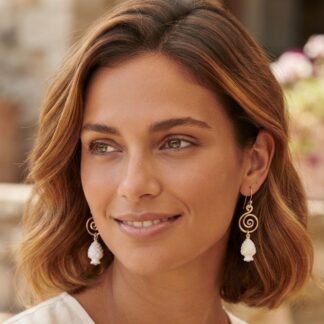 Close-up portrait of a woman with shoulder-length brown hair wearing gold spiral earrings with white bead drops.