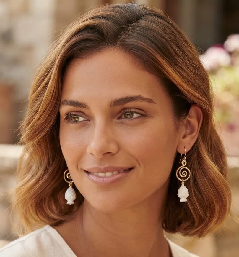 1791826975754 - Zanghi collection Close-up portrait of a woman with shoulder-length brown hair wearing gold spiral earrings with white bead drops.