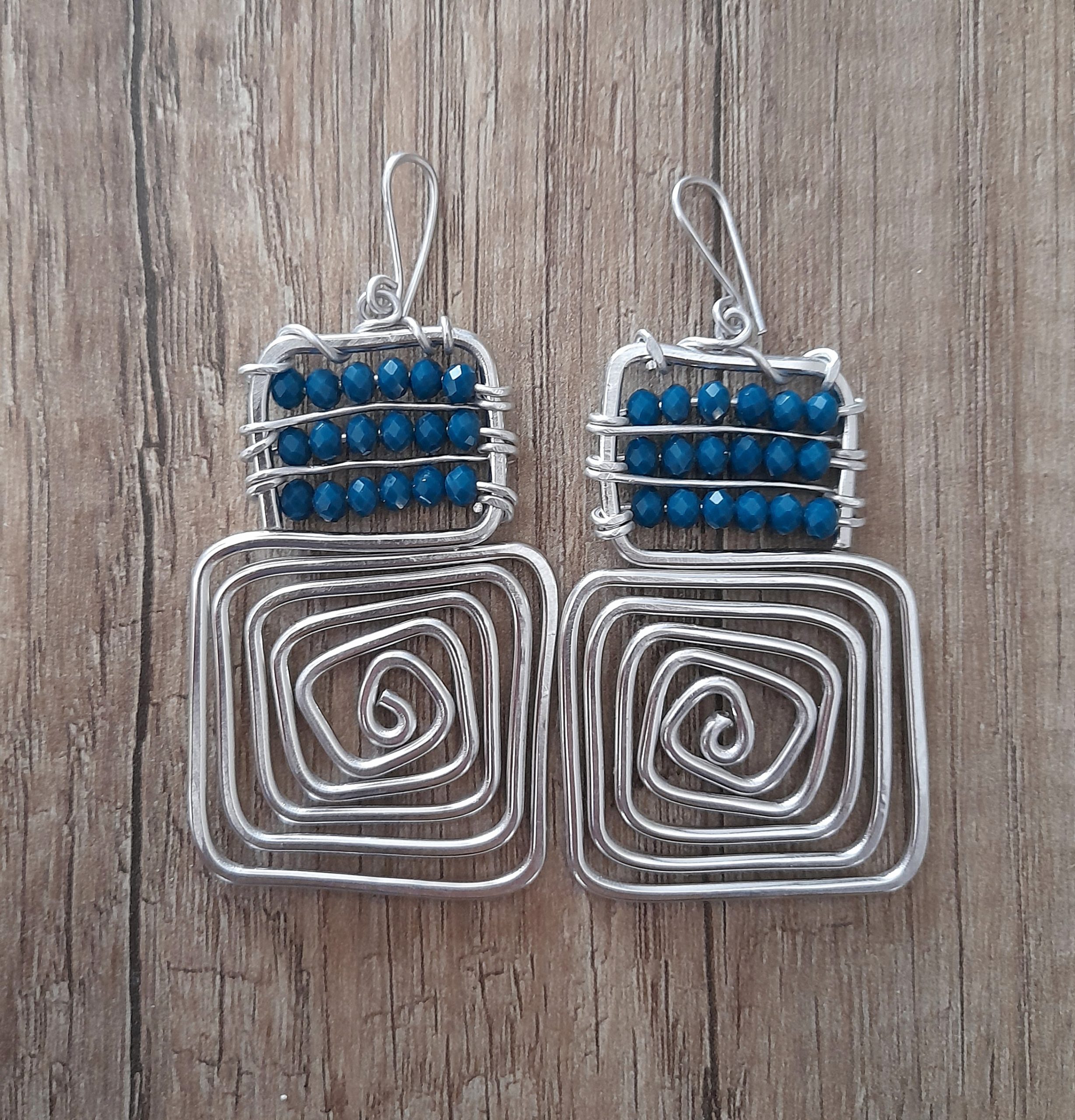 Orecchini artigianali quadrati con perline bluette in vetro sfaccettato, fatti a mano con filo d'alluminio anodizzato . Ganci(monachelle) antiallergici, artigianali 100% alluminio senza nichel ne altri metalli.L'alluminio anodizzato è un metallo che non si ossida anche se a contatto con acqua profumo o detergenti. leggerissimo ed antiallergico.Acquistando questo prodotto non compri un semplice oggetto, ma ore di lavoro, prove e fallimenti, un po' del mio tempo, amore e passione che dedico ad ogni mia creazione.Misura: 76x36mm Peso: 12 grammi - Zanghi collection Orecchini artigianali quadrati con perline bluette