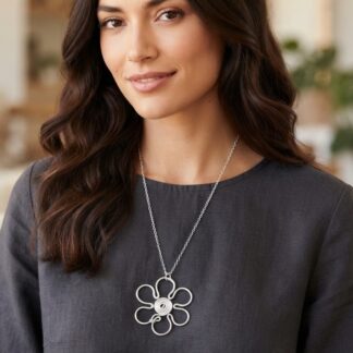 1791746256311 - Zanghi collection Woman with dark wavy hair wearing a gray top and a silver flower-shaped pendant necklace on a chain.
