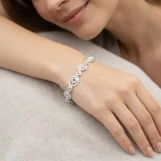 Close-up of a woman’s wrist wearing a silver spiral bracelet resting on a beige cushion.
