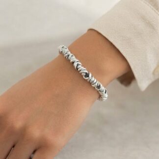 Close-up of a wrist wearing a twisted silver bracelet on a beige sleeve.