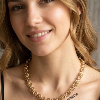 Smiling woman wearing a gold chain necklace; tattoo reads 'FELC' with two stars on her collarbone.