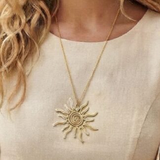 Gold sunburst pendant necklace hanging on a delicate chain over a beige top, close-up view.