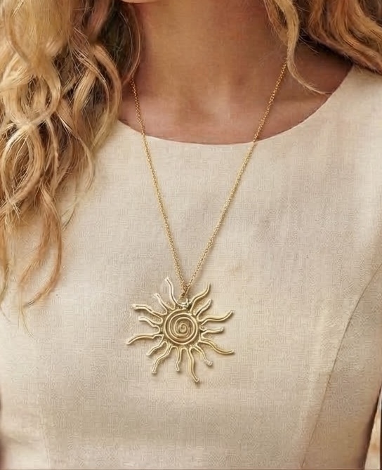 1790750192810 - Zanghi collection Gold sunburst pendant necklace hanging on a delicate chain over a beige top, close-up view.