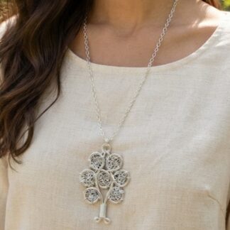 Woman wearing a cream linen top with a silver tree-shaped pendant necklace featuring circular filigree accents on the branches.