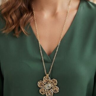 Gold-tone flower pendant necklace with intricate filigree worn over a green blouse, chain resting at the chest.