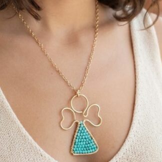 Gold chain necklace with a clover-shaped pendant and a turquoise triangular bead charm, worn over a light beige top.