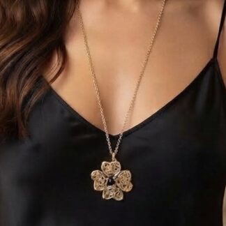 Gold flower pendant necklace with five petals and small stones, worn on a thin chain against a black top.