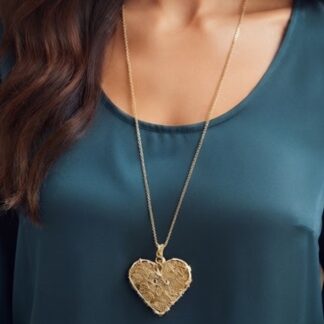 Close-up of a gold heart pendant on a chain resting on a teal blouse.